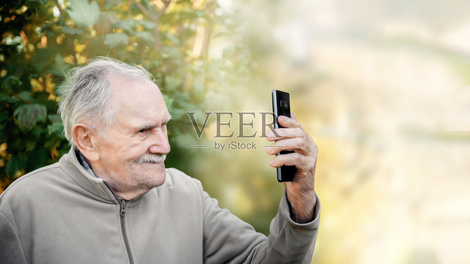 上了年纪的活跃的英俊男子用一部手机自拍。一位老人看着镜头，一边说一边笑。复制空间,旗帜。照片摄影图片