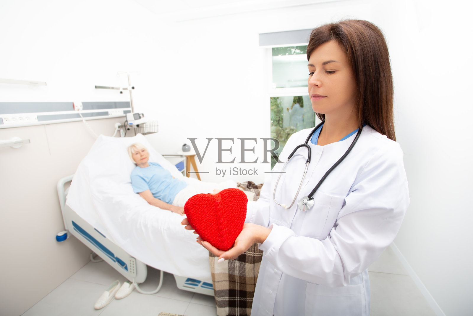 在医院里照顾一位老年病人。医生拿着一个心脏模型。心脏病学，心脏病患者的医疗护理。心脏病发作，治疗，康复照片摄影图片