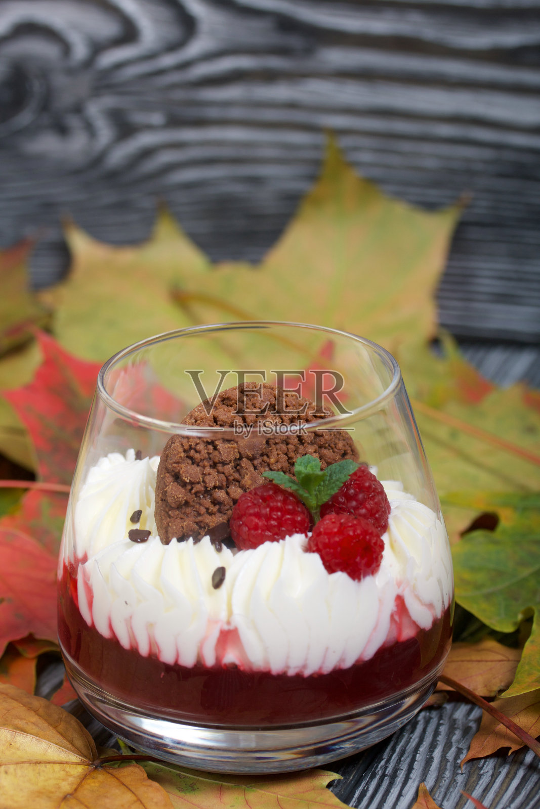 奶油奶酪和覆盆子果冻制成的甜点。装饰饼干，覆盆子和薄荷。到处都是干燥的秋天枫叶。照片摄影图片