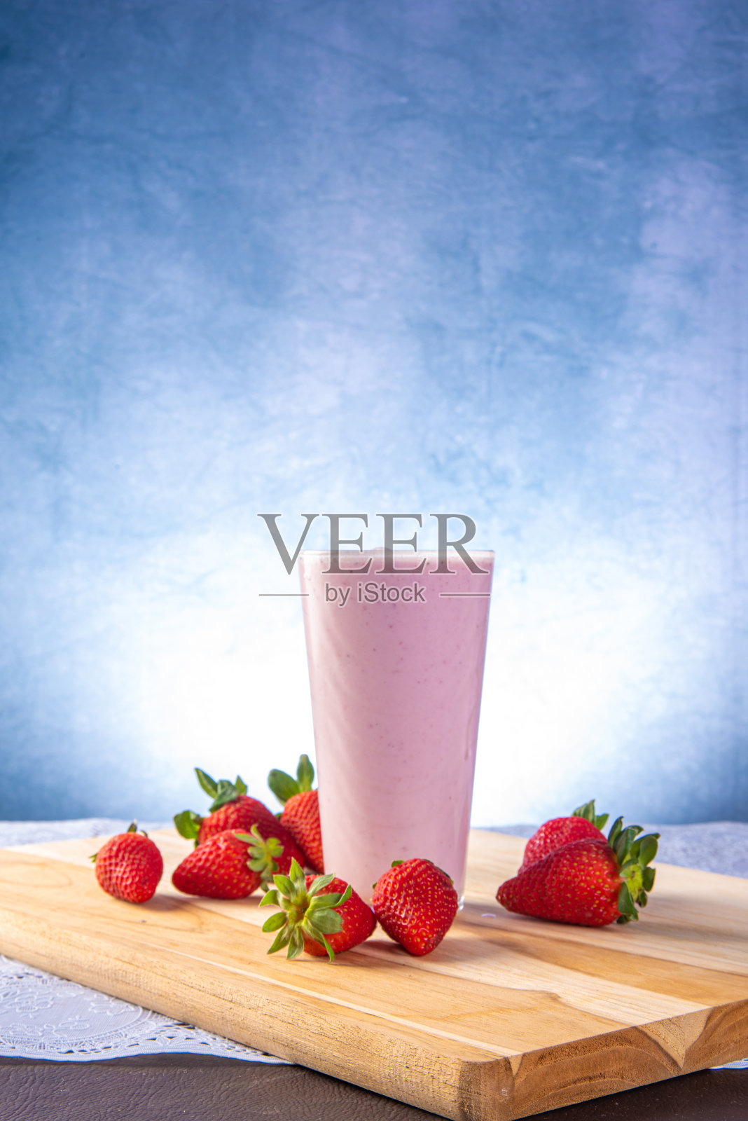 草莓汁放在玻璃杯里，周围是草莓，蓝色渐变背景，选择性聚焦。照片摄影图片