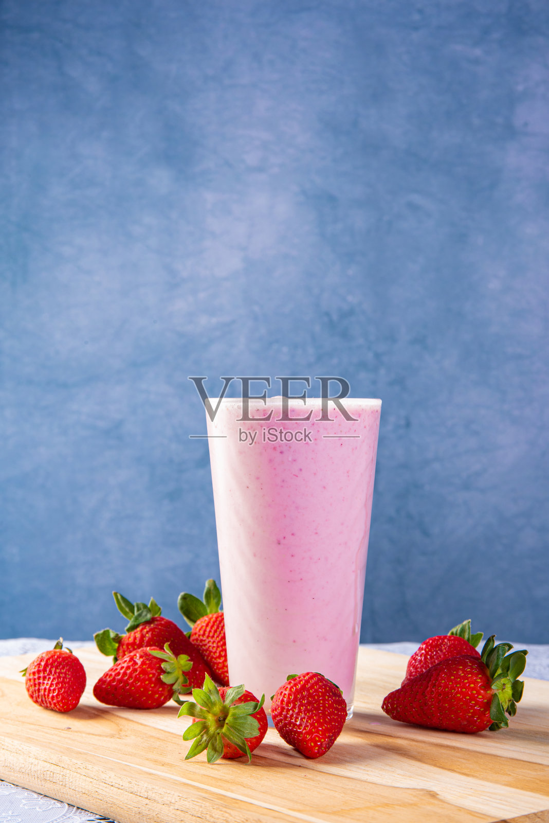 草莓汁放在玻璃杯里，周围是草莓，蓝色渐变背景，选择性聚焦。照片摄影图片