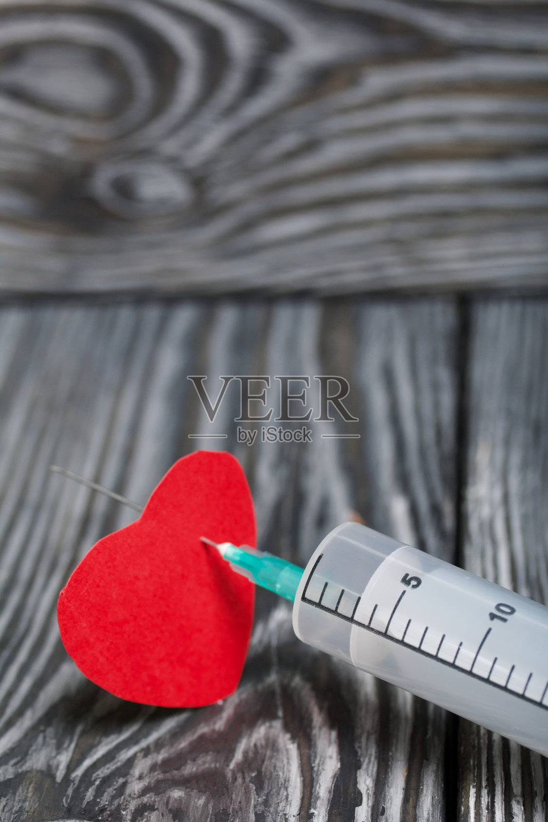 一颗被医用注射器穿刺的纸心脏。以黑色松木板为背景。照片摄影图片