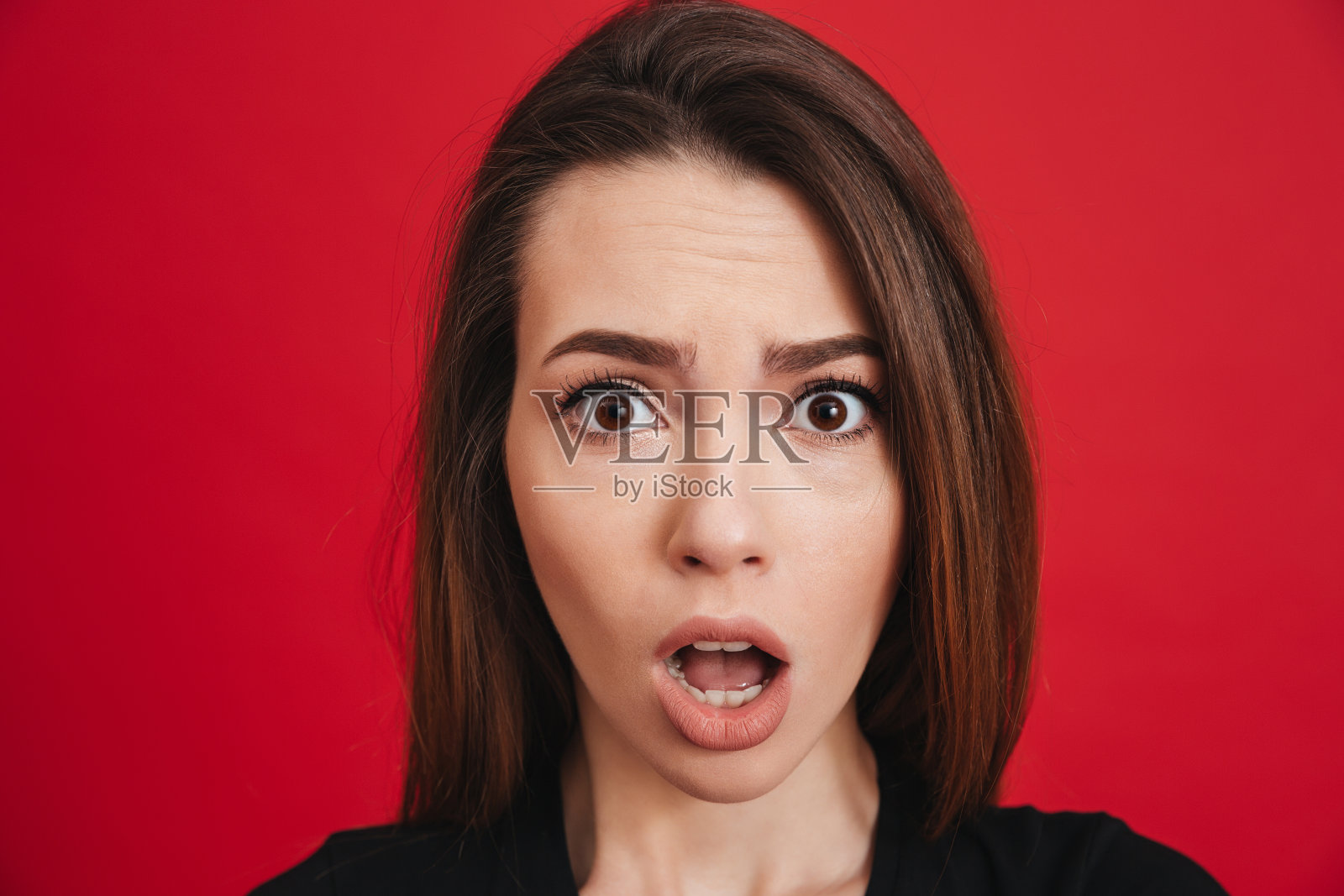 20多岁的困惑女性在镜头前张大嘴巴，兴奋或震惊，孤立在红色背景下照片摄影图片
