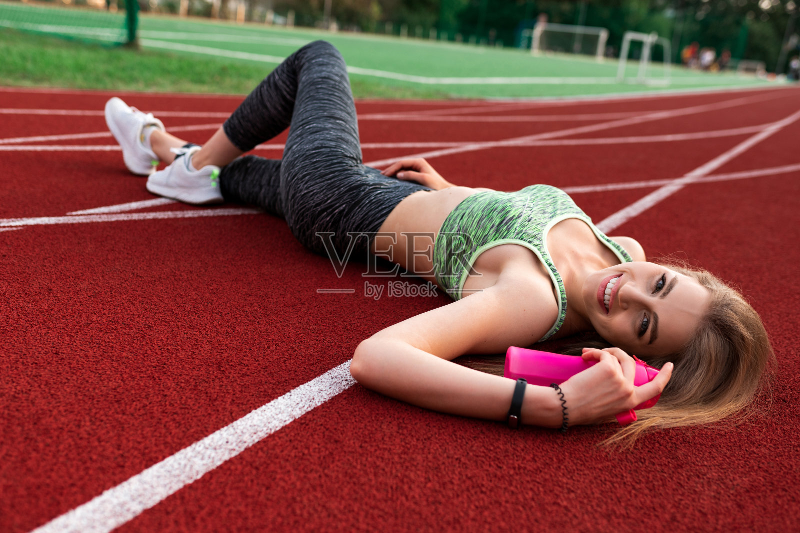 一个身体健康的女人躺在跑道上，手里拿着一瓶水照片摄影图片