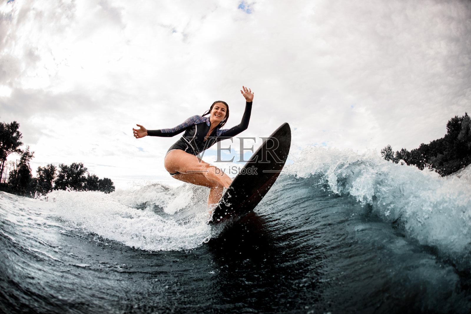积极开朗的女人穿着黑色潜水衣有效地骑在冲浪板上照片摄影图片