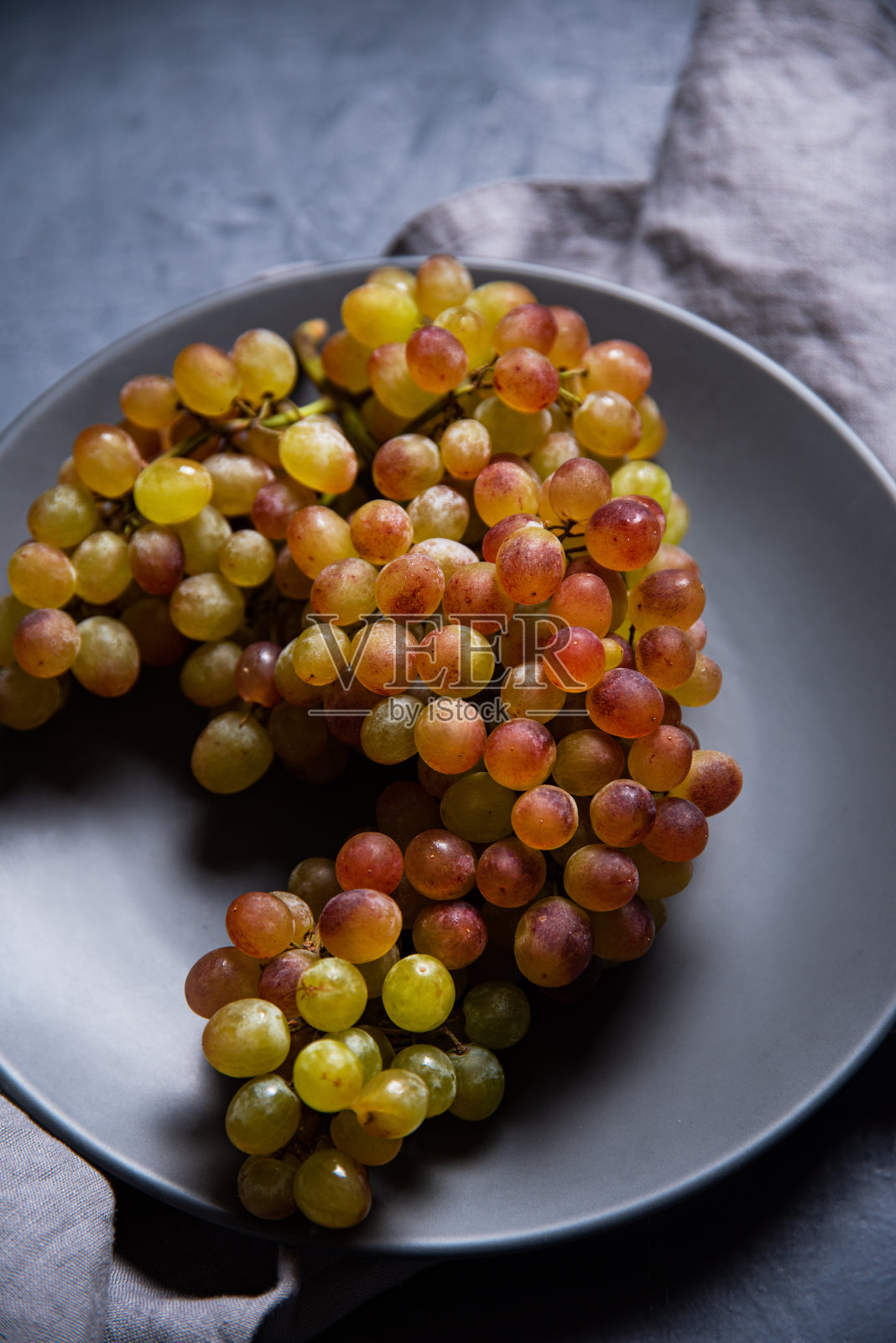 深灰色的桌子上，灰色的盘子里放着一串多汁的绿粉色葡萄照片摄影图片