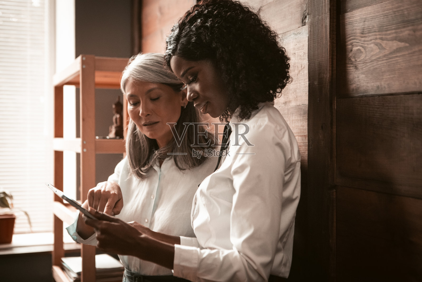 两位商业女性在使用数字平板电脑。成熟的亚洲女性和年轻的非洲女性一起工作。彩色图像。高质量的照片照片摄影图片