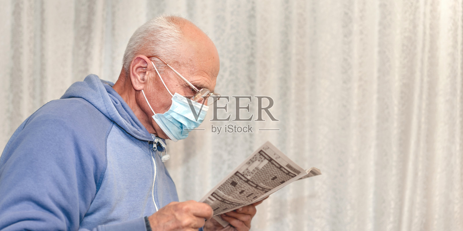戴着眼镜和医用口罩在医院或养老院看报纸的老年人照片摄影图片