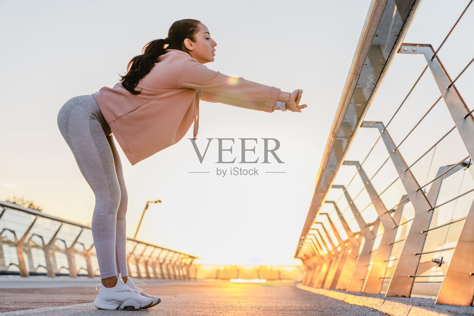 苗条的女孩穿着运动服在清晨的桥上训练照片摄影图片