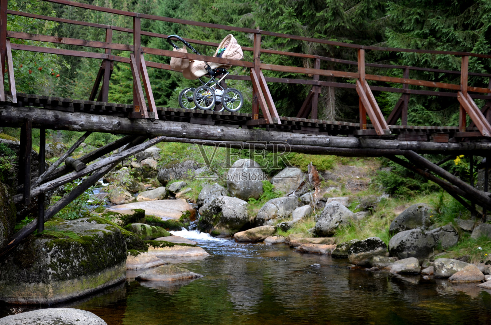 在木桥上推着婴儿车，用巨大的花岗岩穿过山间小溪。泥炭、铁、水和苔藓创造了海湾和峡湾的图像照片摄影图片