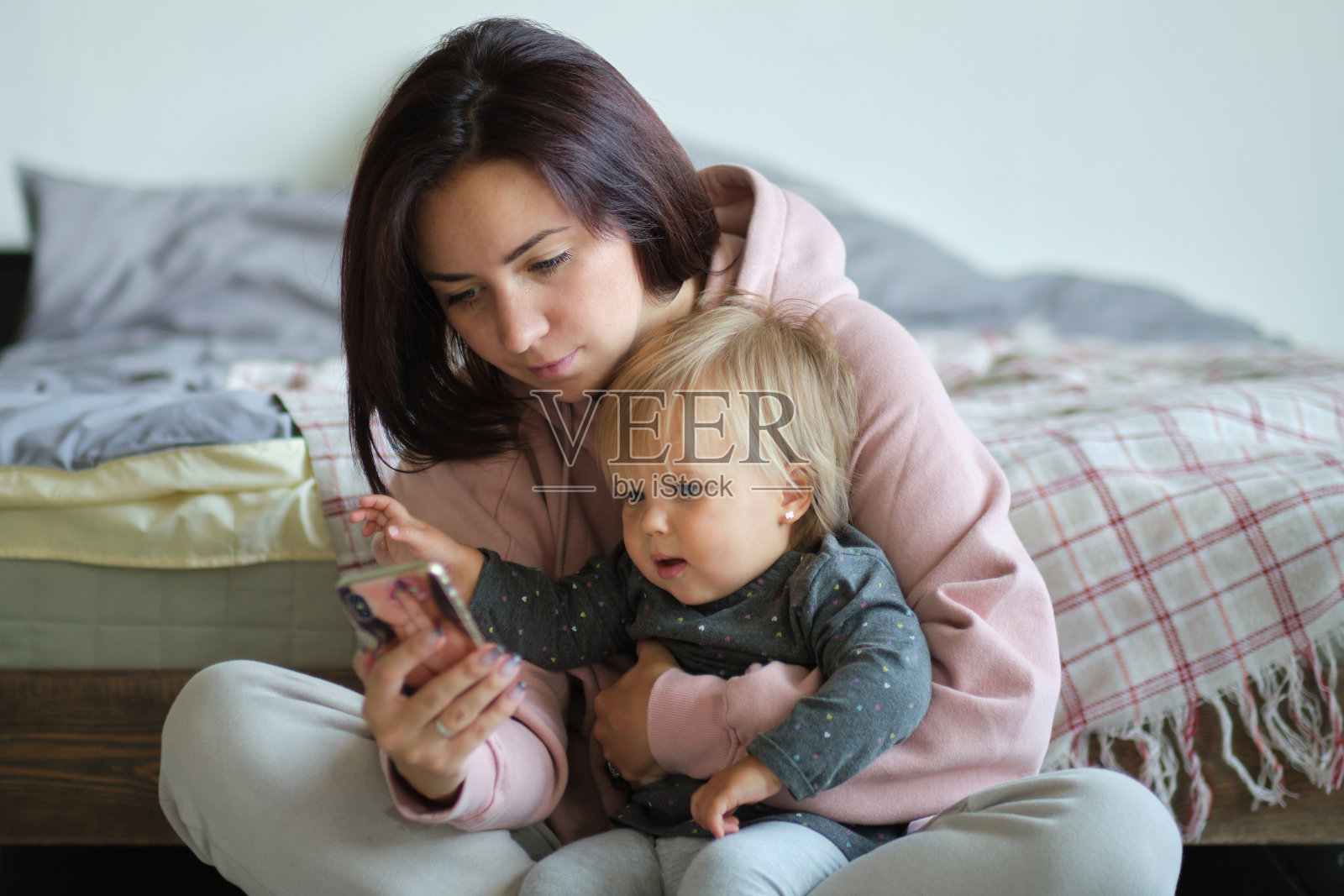 小女孩和妈妈坐在床上看智能手机上的卡通，玩游戏。孩子通过视频与祖母交谈。妈妈给女儿看手机屏幕上的照片照片摄影图片