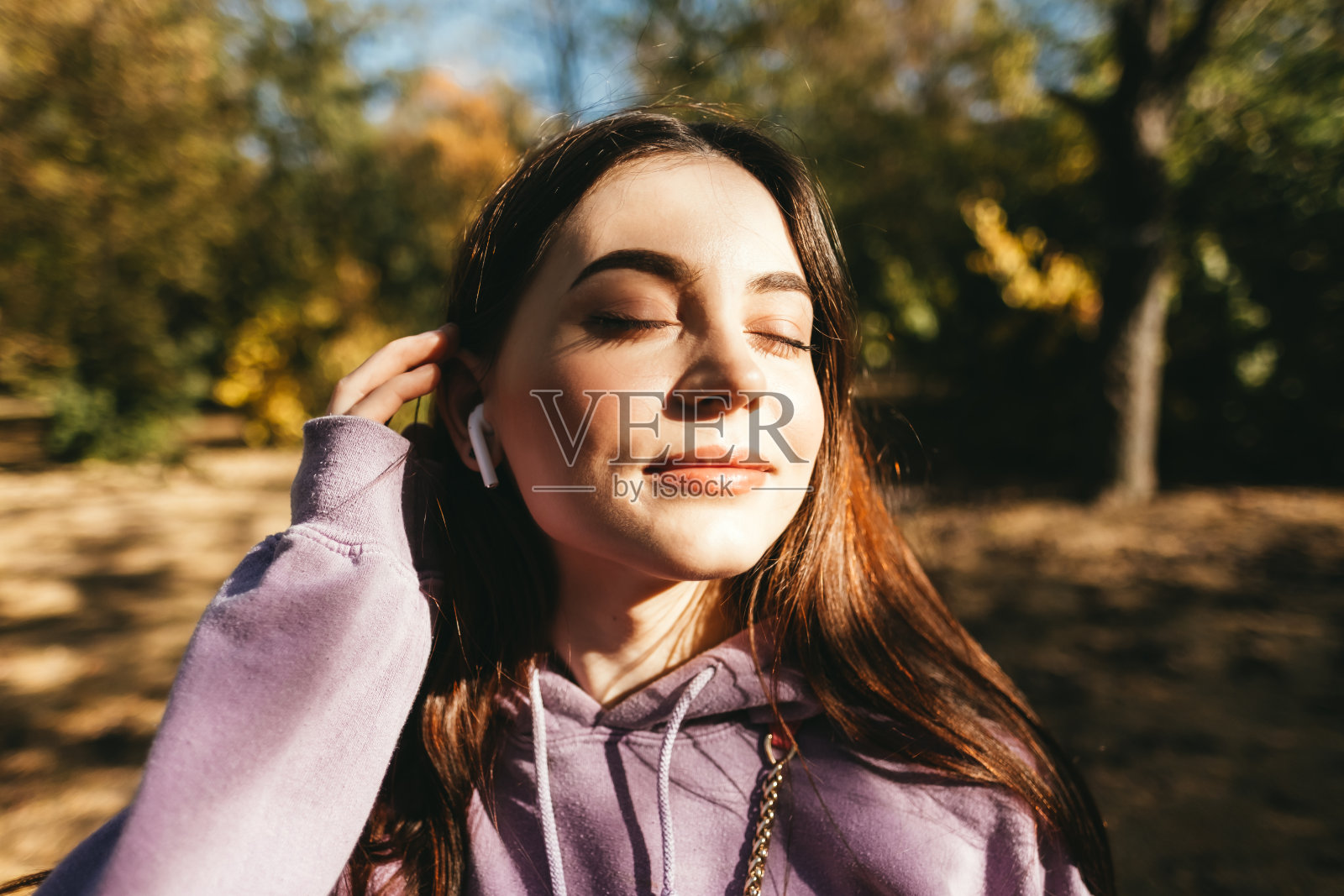 年轻女子戴着耳机在公园里听音乐，享受秋天的天气。照片摄影图片