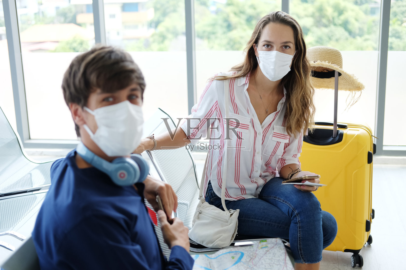 年轻的白种旅客情侣爱戴口罩预防covid-19病毒正在机场一起坐在候机座位上。医疗保健蜜月旅行度假概念。照片摄影图片
