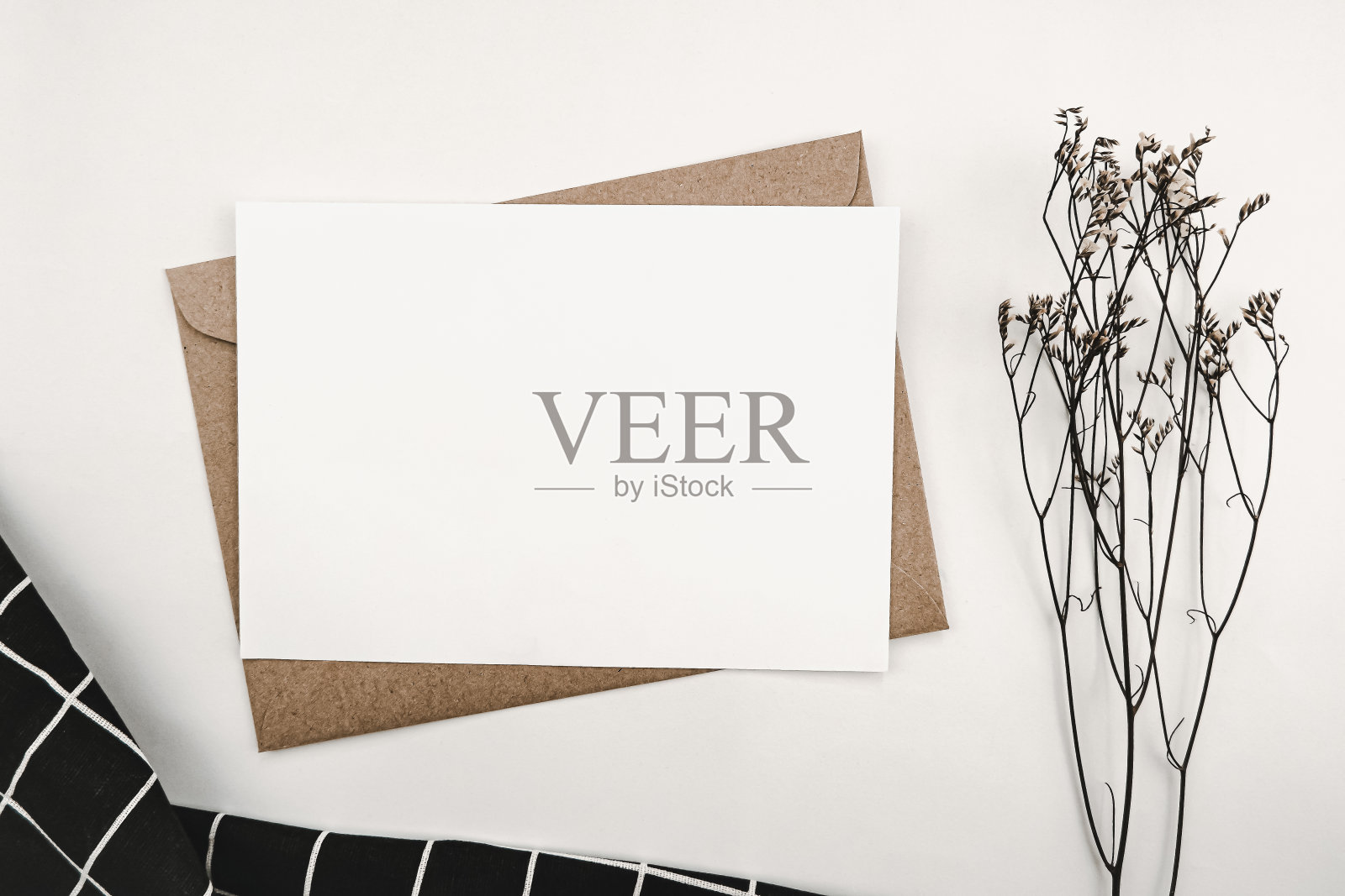 空白白纸在牛皮纸信封与补草干花和黑布与白色网格图案。模拟水平空白贺卡。顶视图的工艺信封上的白色背景。照片摄影图片