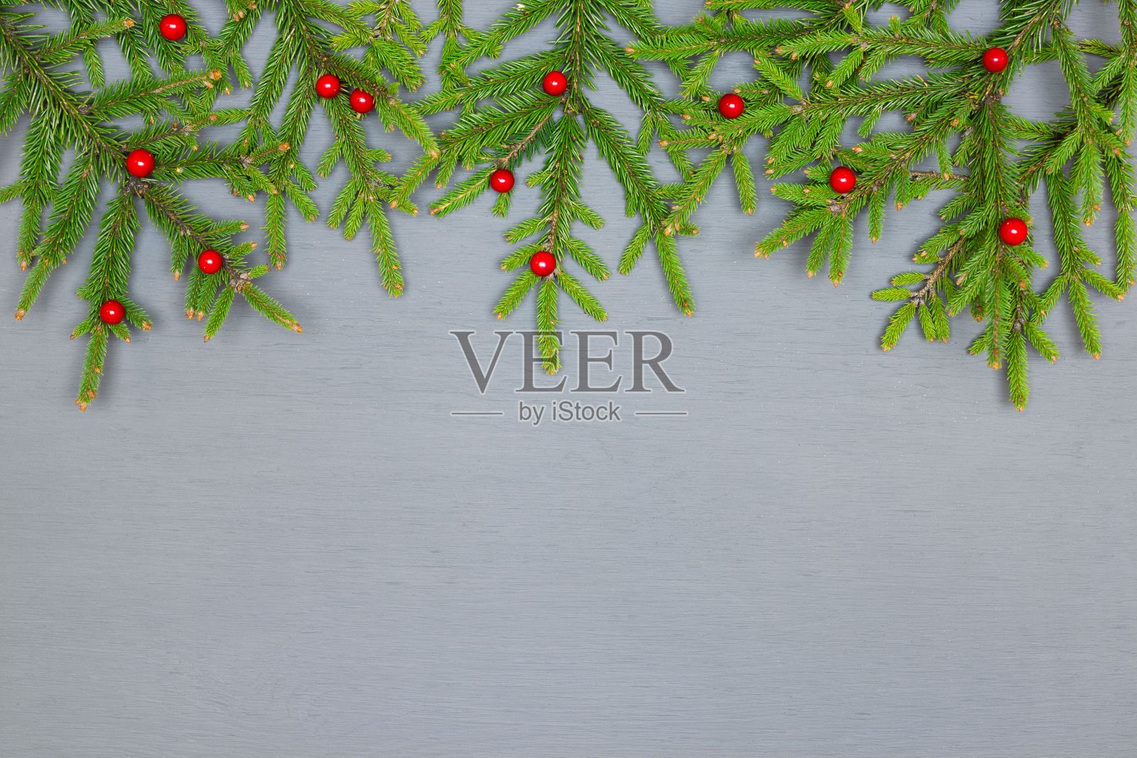 绿色的圣诞树树枝与红色冬青冬青浆果在灰色油漆木材与复制空间。圣诞帧背景照片摄影图片