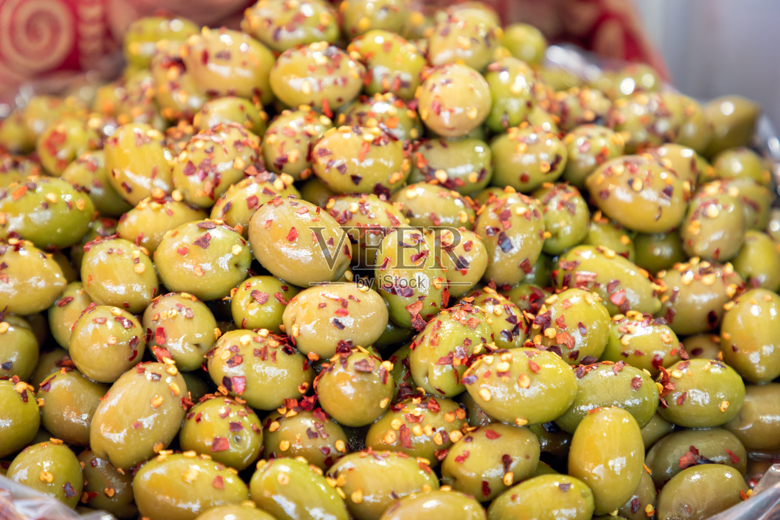 一堆撒着红辣椒的咸绿橄榄。食品市场上的加香料的绿橄榄照片摄影图片