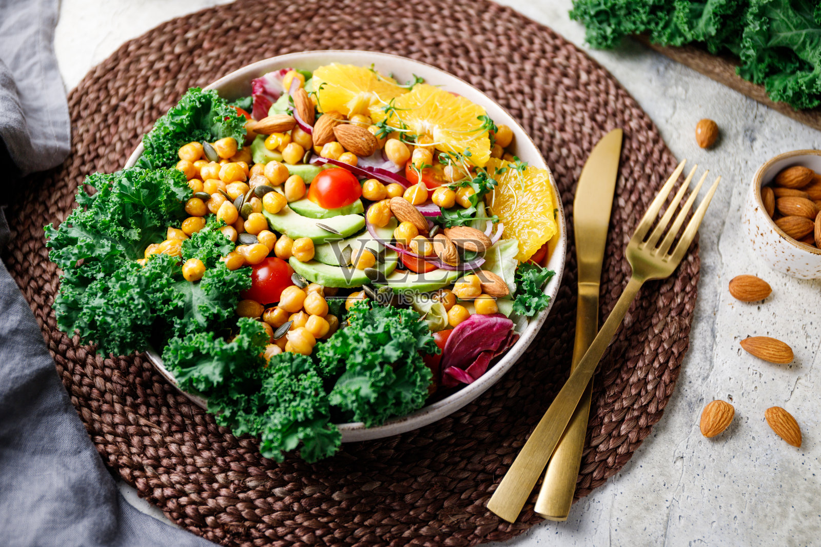 健康的素食沙拉，有鳄梨，鹰嘴豆，新鲜羽衣甘蓝，罗马诺叶，樱桃番茄，杏仁。洋葱和橙色。照片摄影图片
