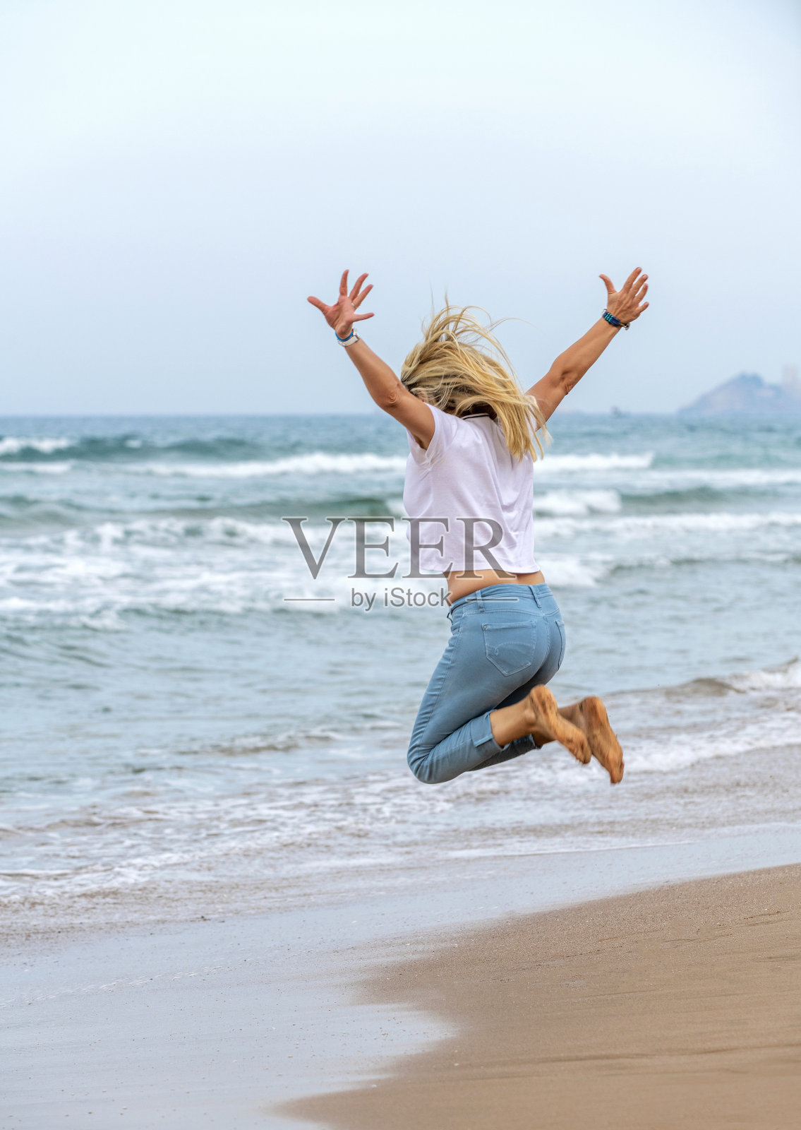 快乐的成年金发女人在海边跳照片摄影图片