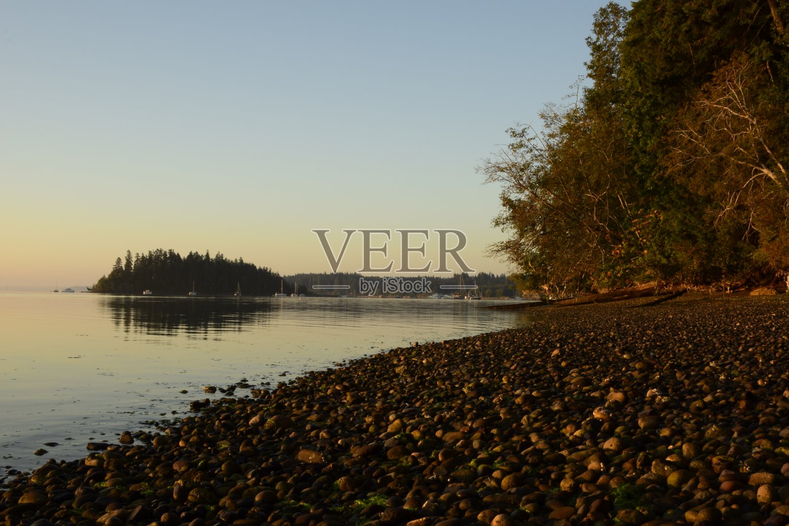 低角度观看宁静的卵石滩对反射水在日出照片摄影图片