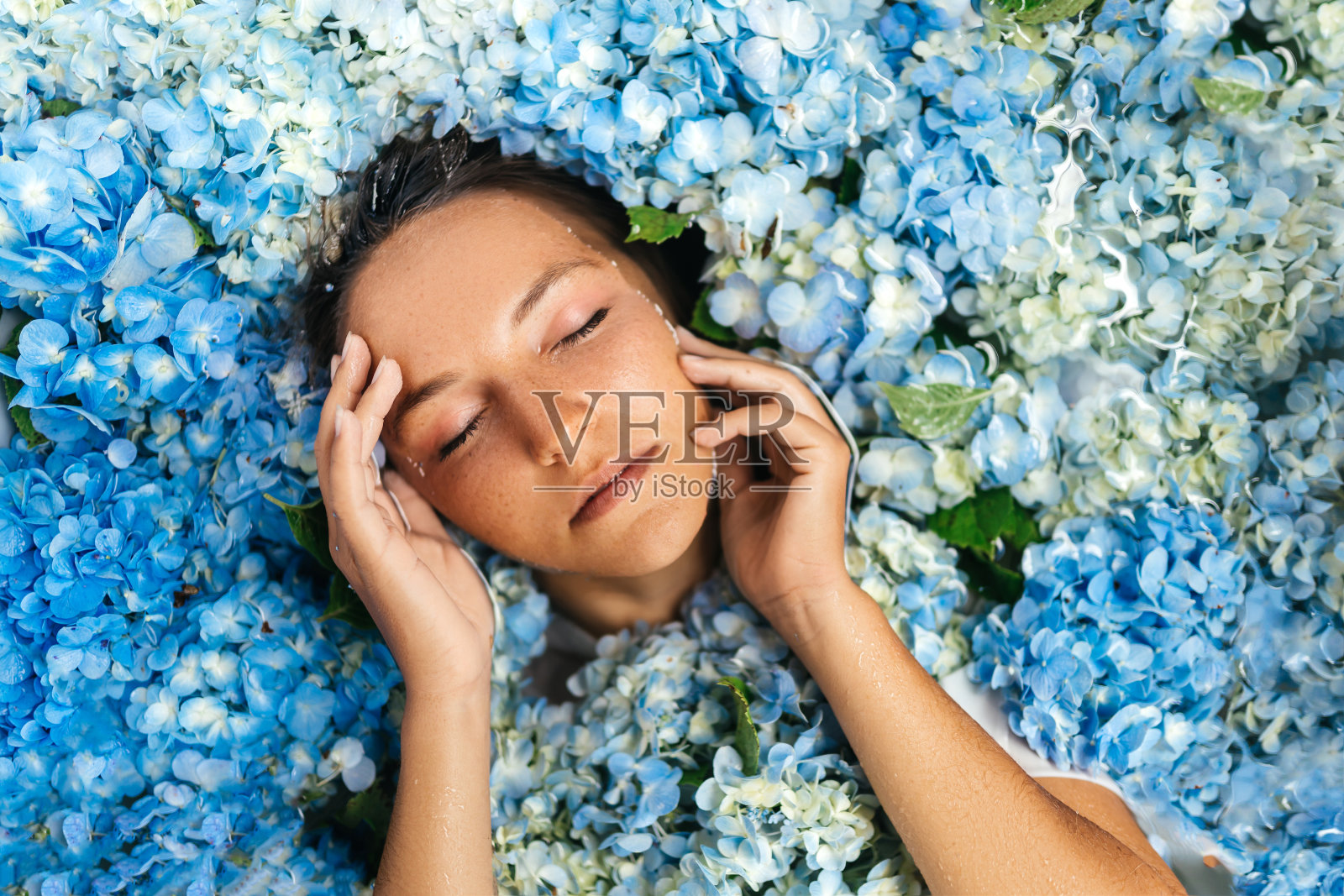 女人放松浴与热带蓝色绣球花。照片摄影图片