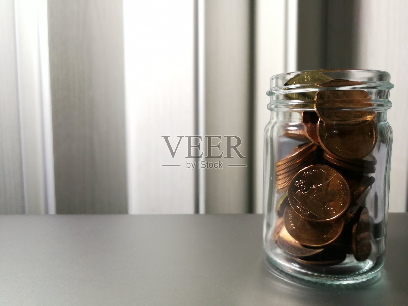 桌子上的玻璃罐中硬币，背景是PVC折叠门照片摄影图片