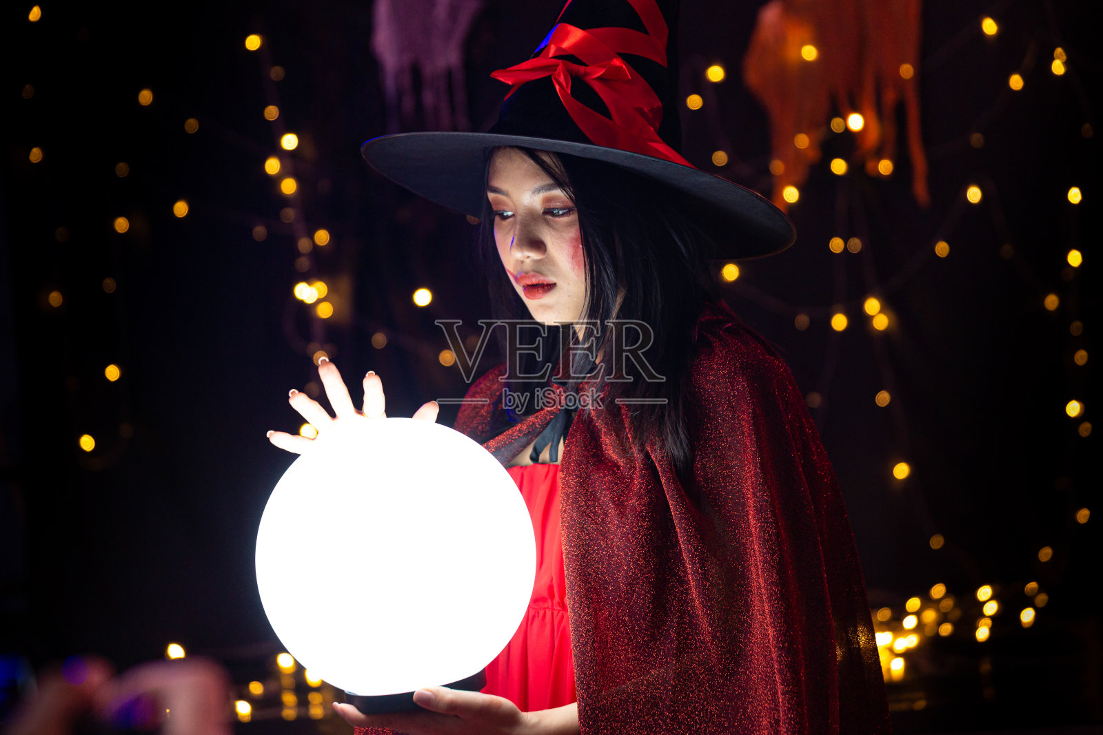 万圣节前夕穿着女巫服装拿着水晶球的女人。万圣节的节日。照片摄影图片