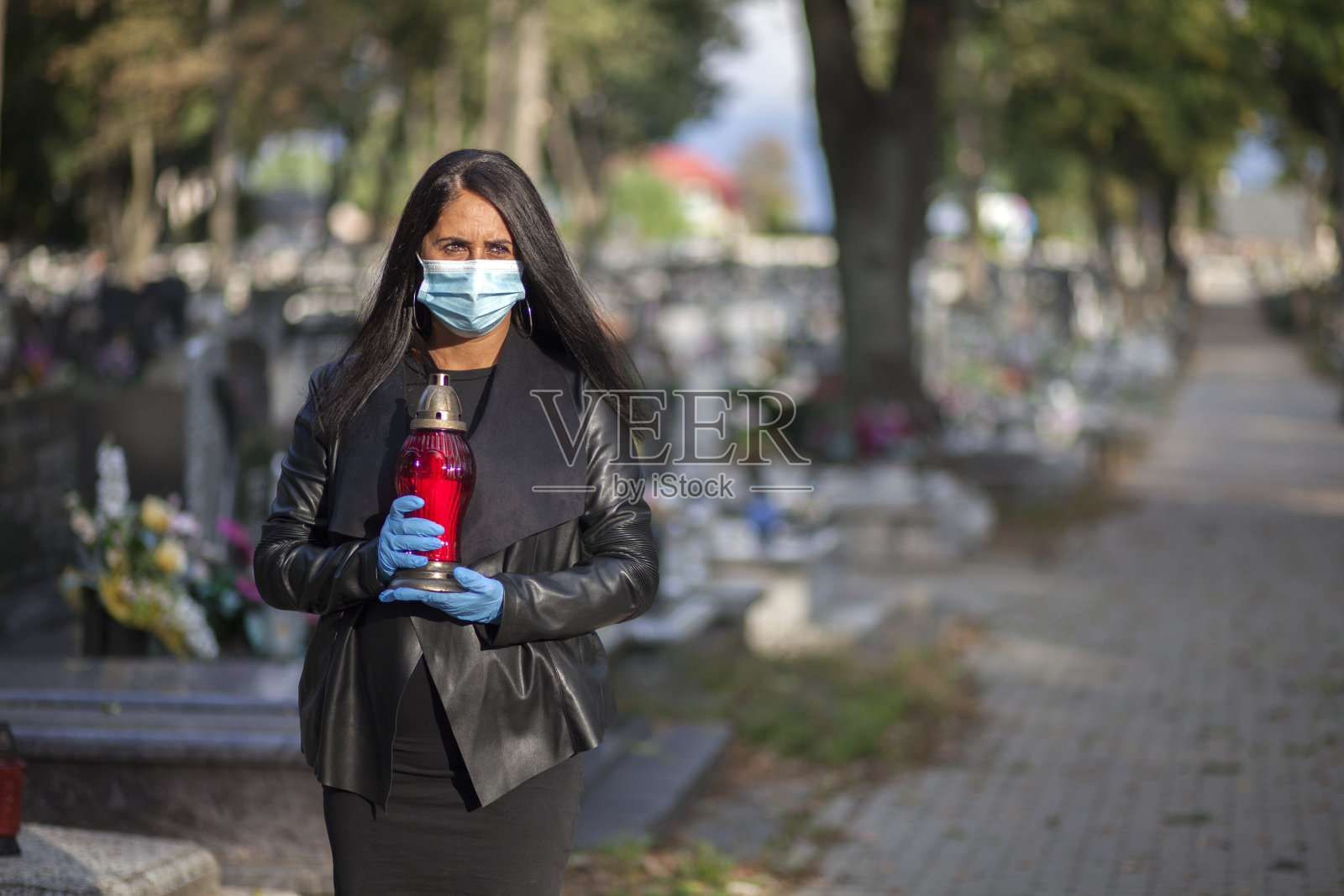 一名妇女戴着防护口罩，手拿蜡烛到墓地探望亲人。封锁公墓照片摄影图片