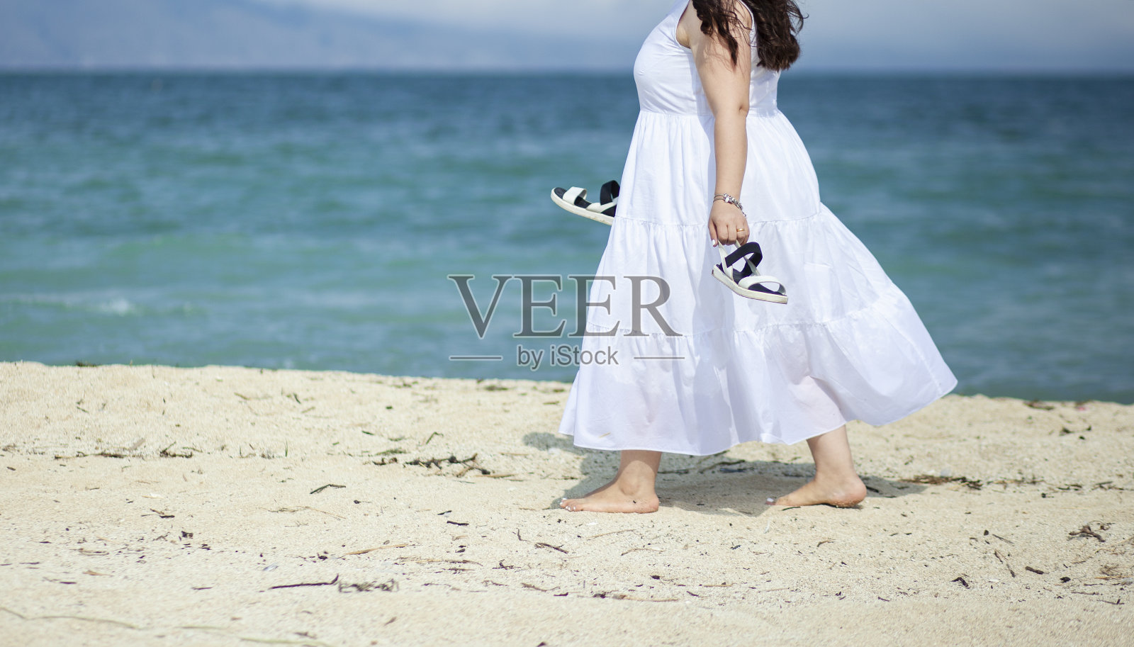 一个女人手拿鞋子走在海滩上照片摄影图片