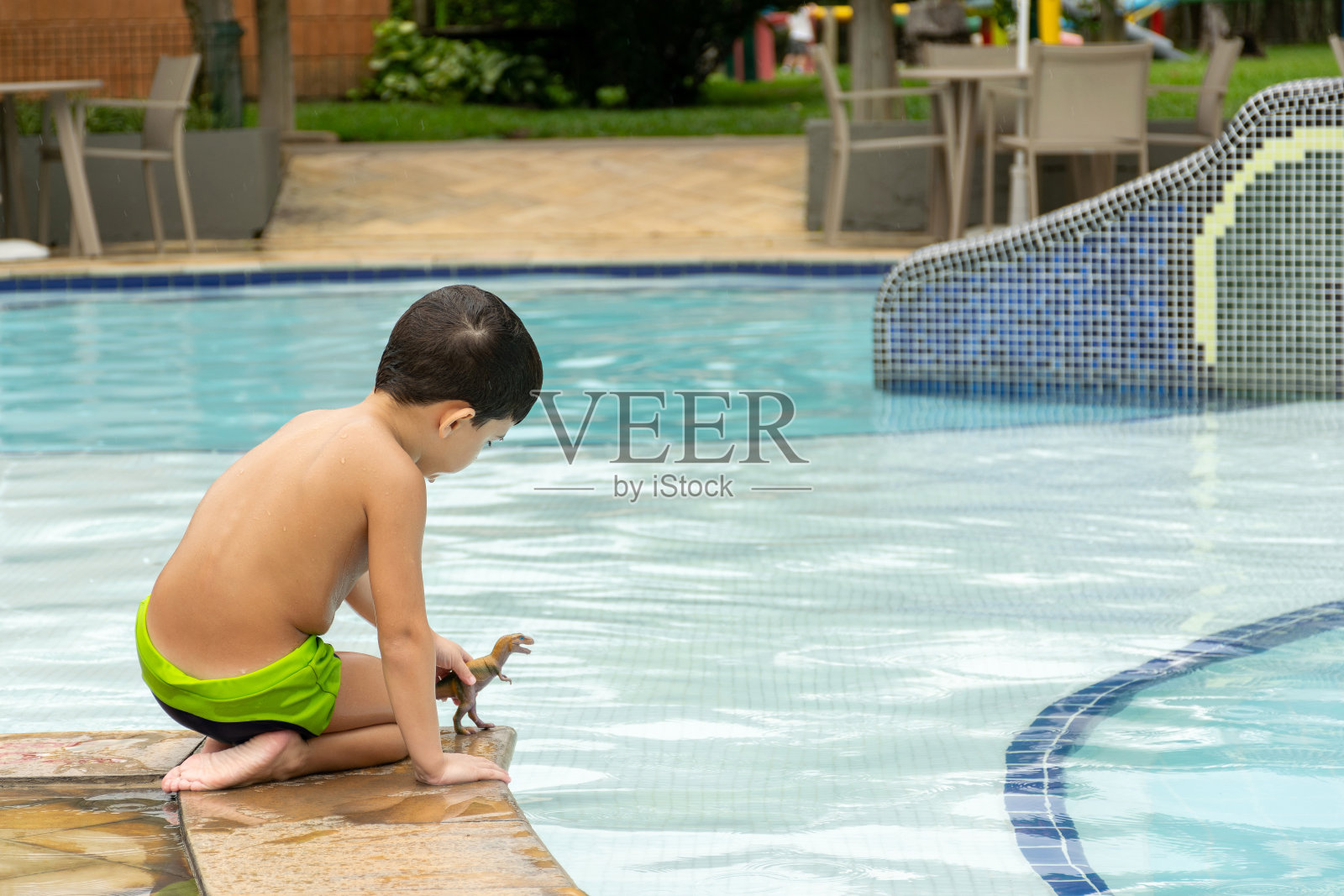 6岁的小男孩，背着他，在泳池边玩恐龙。照片摄影图片