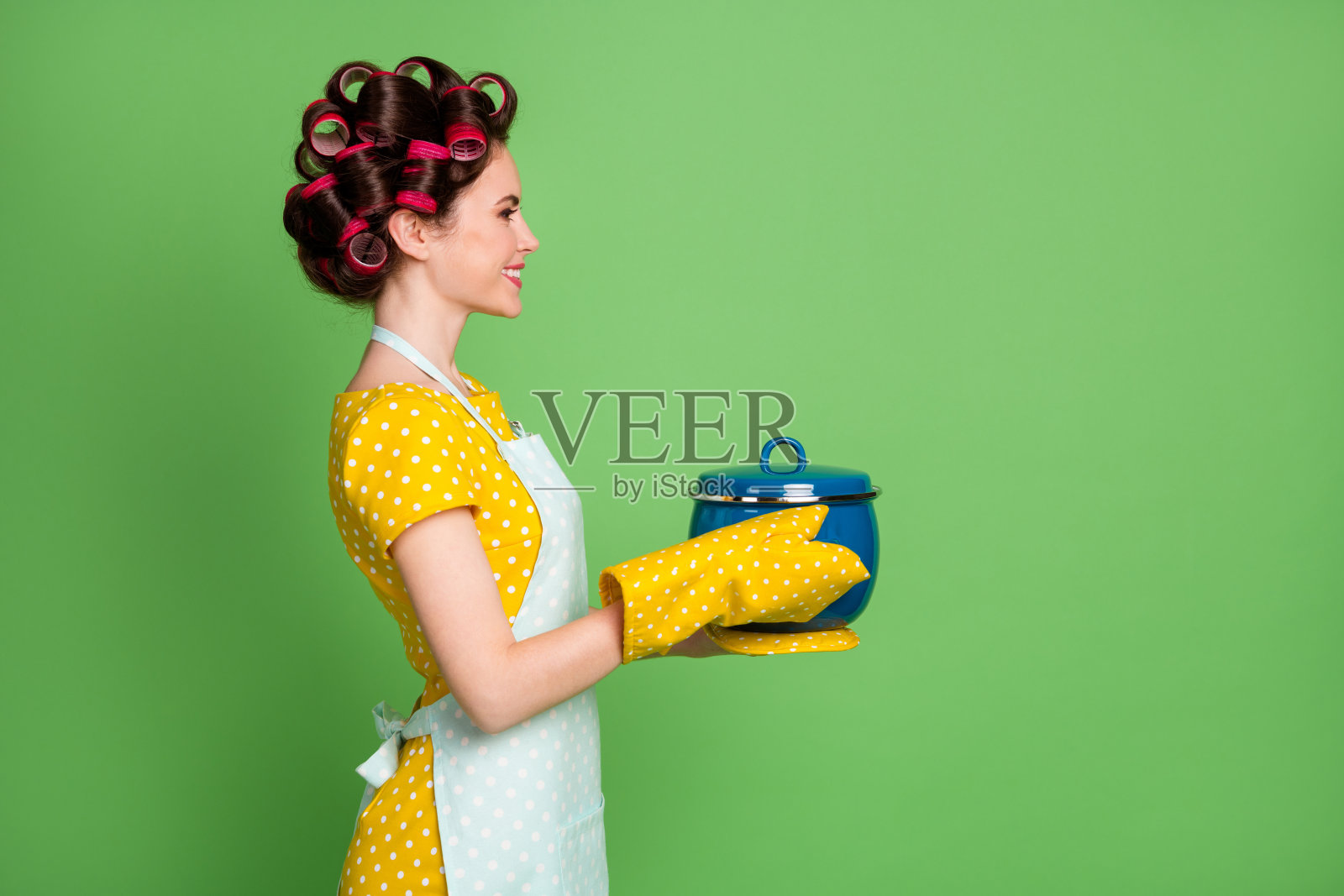 正面女孩的个人资料侧面照片准备美味的汤端炖锅看起来不错的copyspace穿黄色的锅托点裙子连衣裙发卷孤立在绿色的背景照片摄影图片