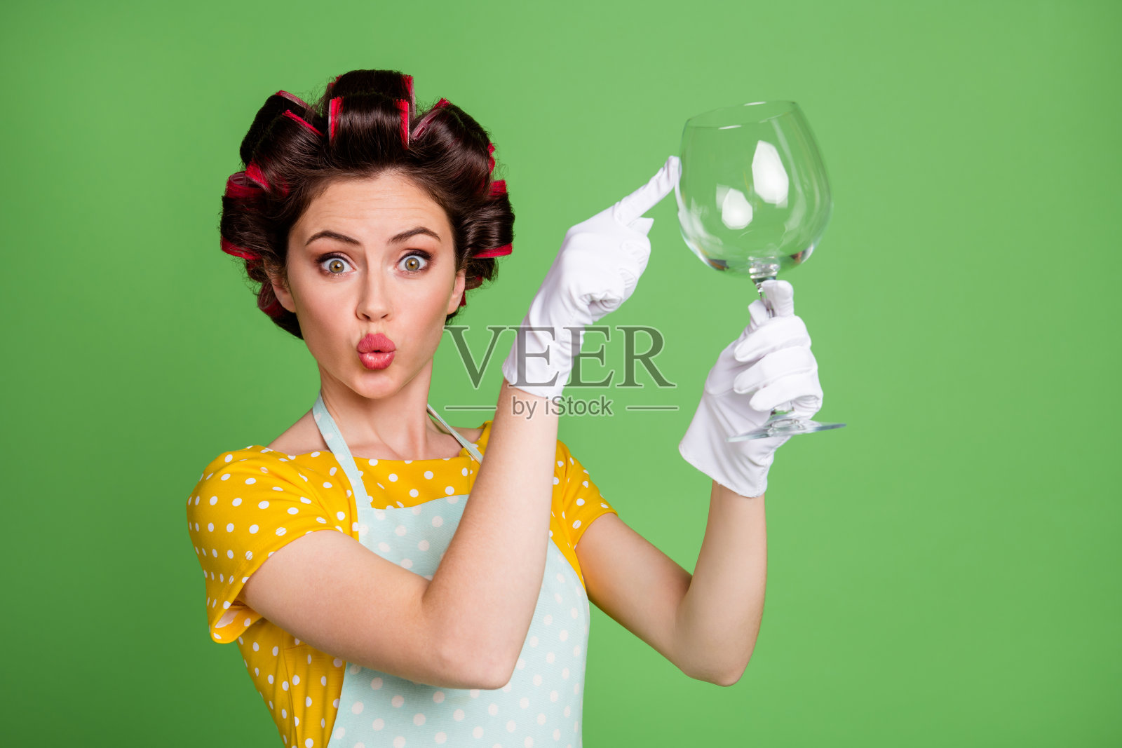 我的天，看干净了。惊讶的复古女孩洗白色的玻璃，印象深刻的触摸手指穿黄色的点裙，时髦的卷发孤立的绿色背景照片摄影图片