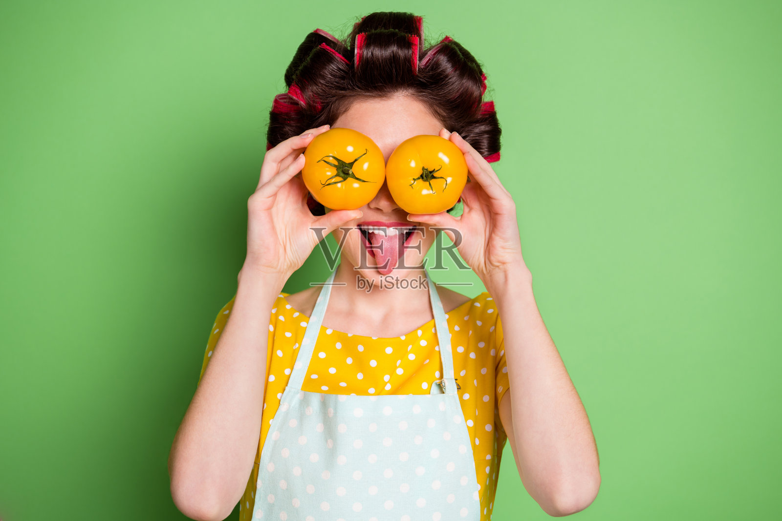 滑稽的疯狂的傻女孩的照片闭上眼睛西红柿准备生态菜穿黄色的斑点t恤围裙发卷孤立在绿色的背景照片摄影图片