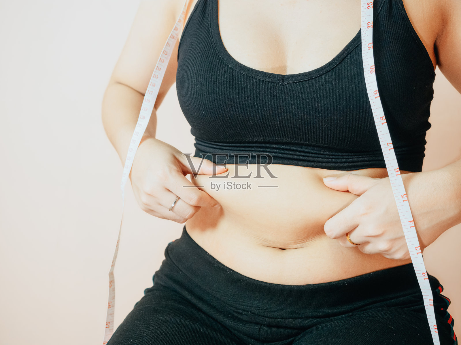 失去腹部脂肪的概念从近距离的妇女在运动服与手握她自己的腹部脂肪和脂肪团。照片摄影图片