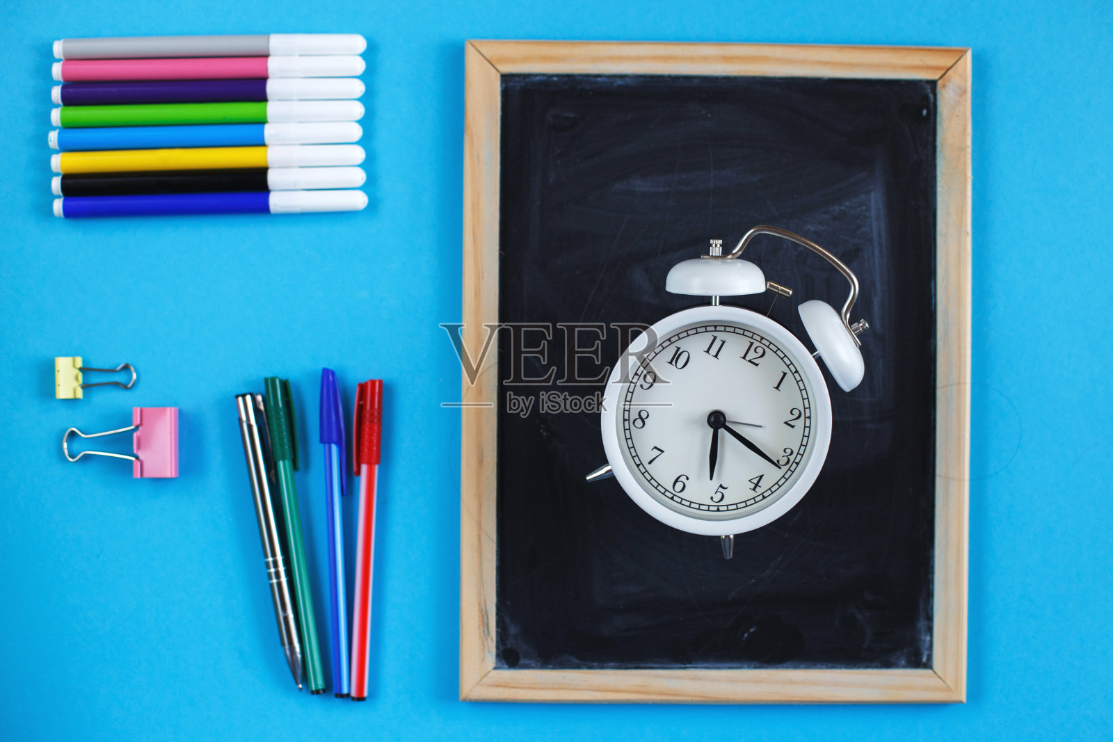 学校黑板和文具配件，铅笔，闹钟和蓝色背景的钢笔。回到学校的概念。照片摄影图片