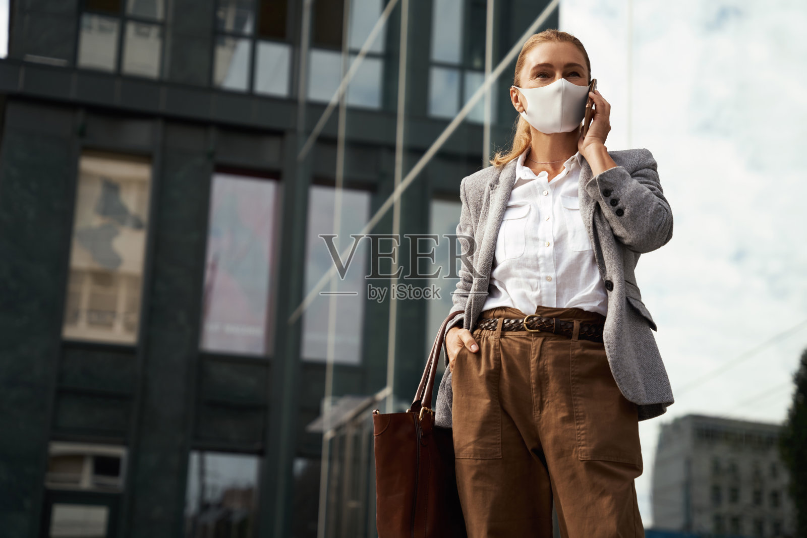 疫情期间的业务。自信的女商人戴着防护面罩在户外对着办公楼讲手机照片摄影图片