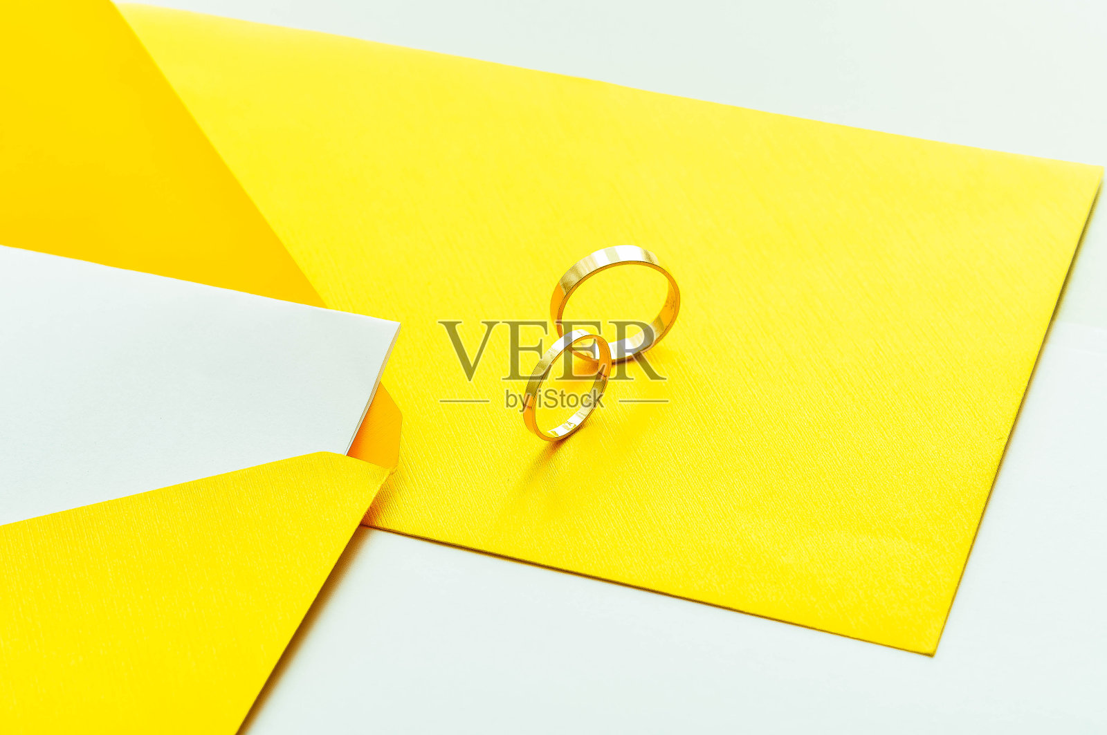 金婚戒上黄色的请柬上白色的背景。照片摄影图片