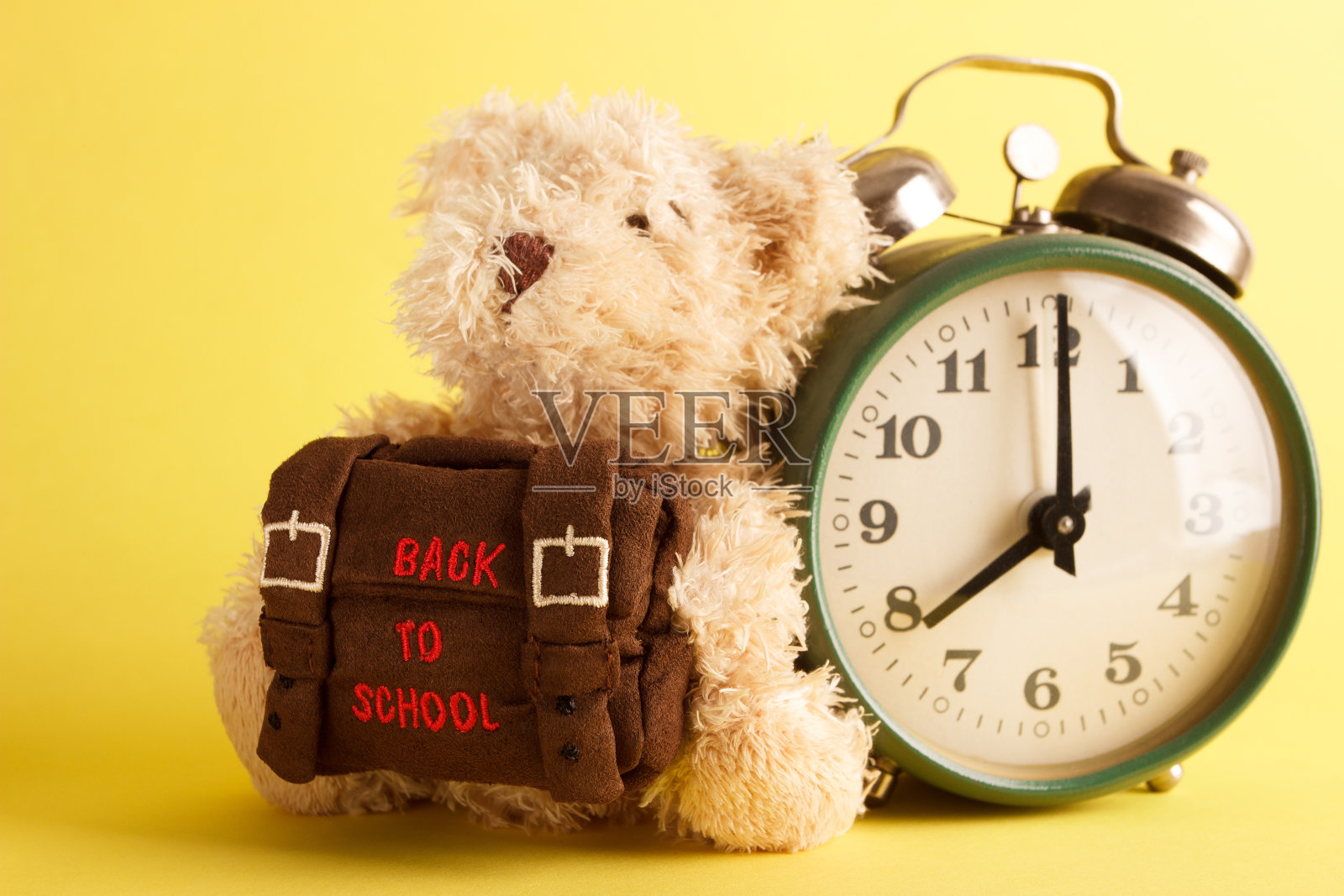 棕色的泰迪熊和学校背包，黄色的背景照片摄影图片