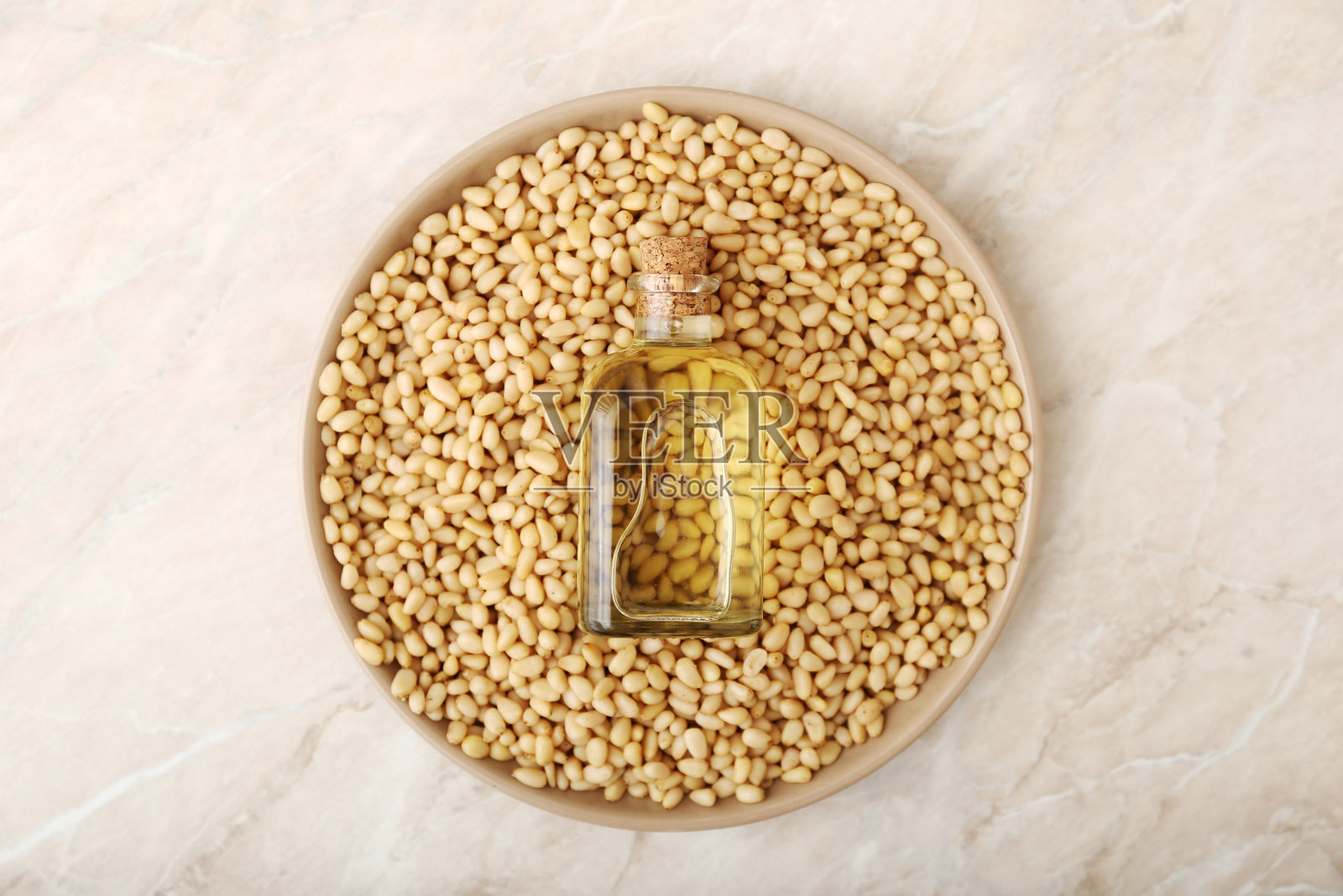 装油的玻璃瓶放在盘子里，配上松子。俯视图上的米色大理石桌子。照片摄影图片