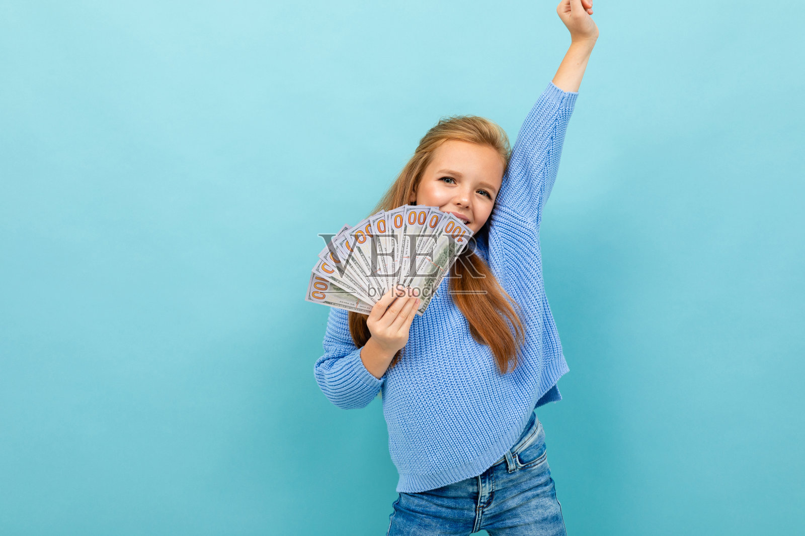 一个迷人的欧洲女孩，手里拿着钱，挂在浅蓝色的墙上照片摄影图片