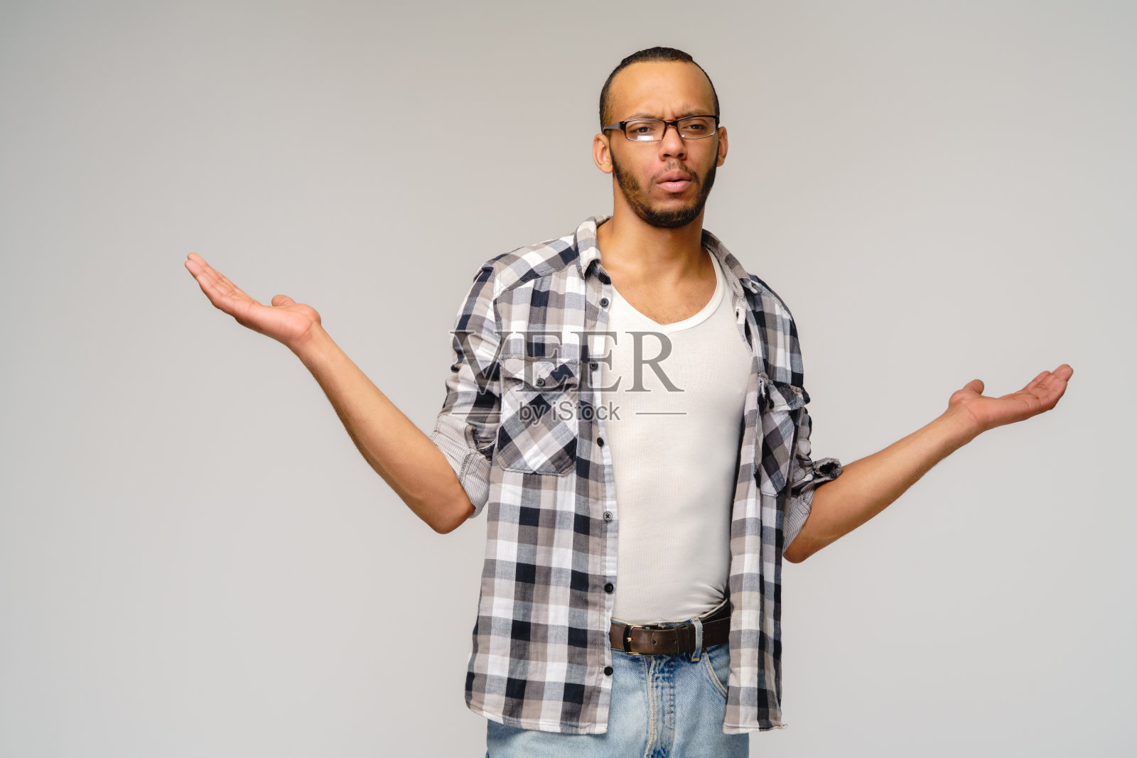 我不知道的手势-一个年轻的非洲裔美国人在灰色的背景下不知所措，手臂和手做着无助的手势，好像他不知道该做什么照片摄影图片