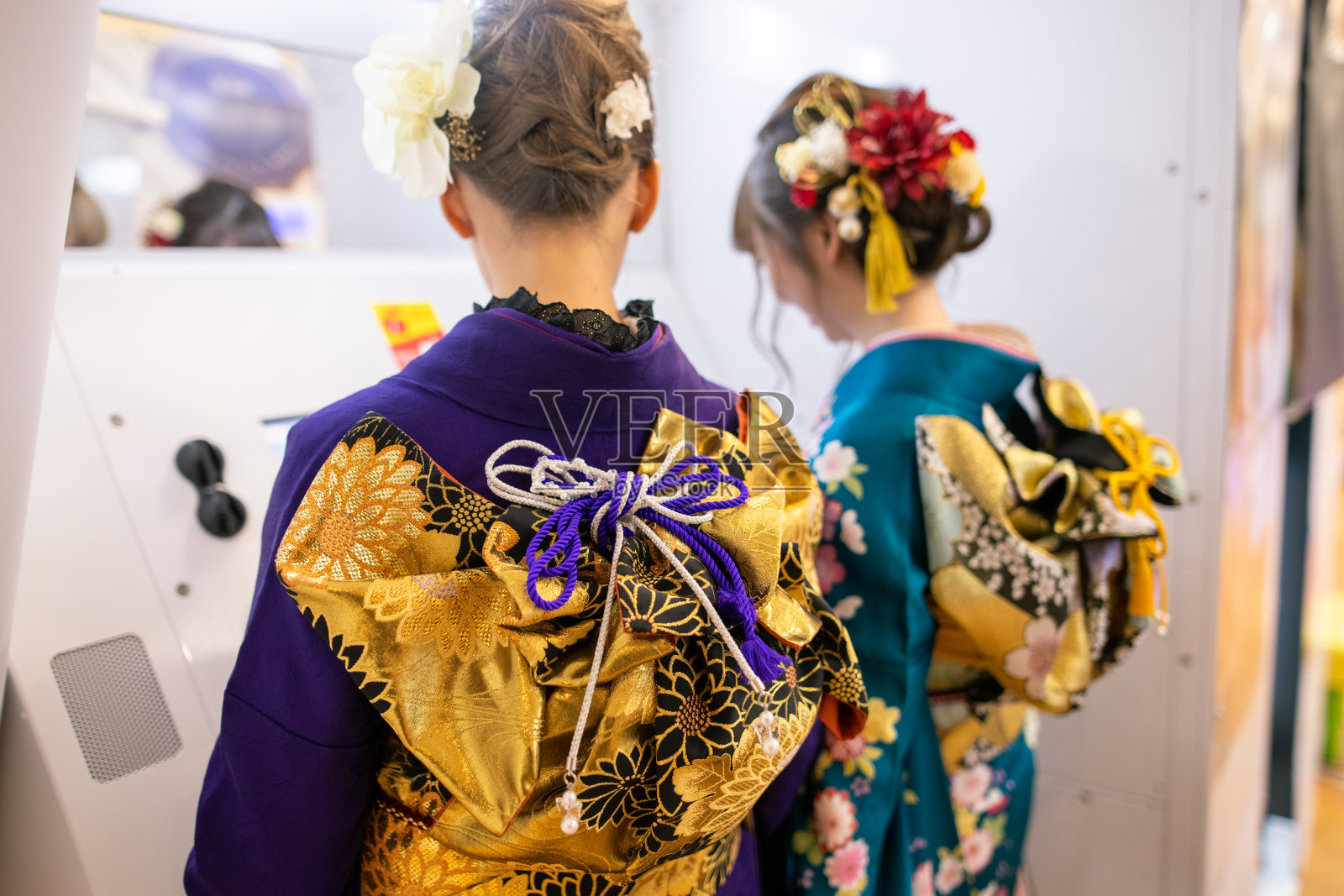 身着Furisode和服的年轻女子在“Purikura”照片贴纸摊上为“Seijin Shiki”成人礼拍照照片摄影图片