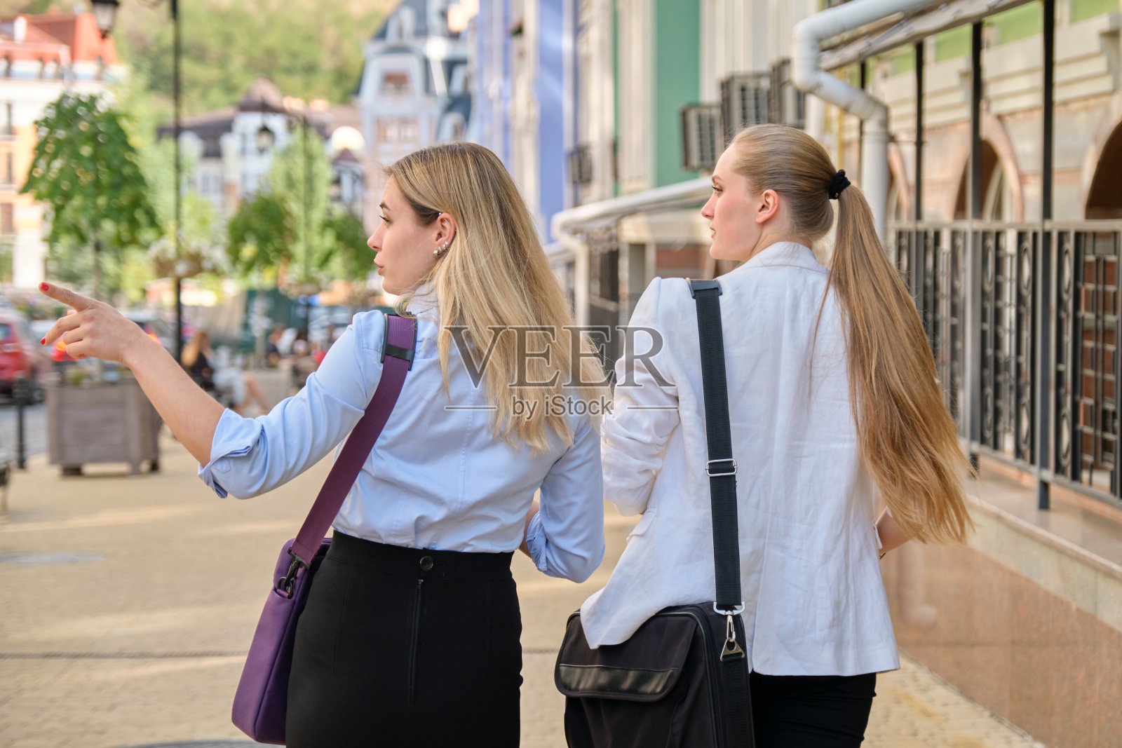 两个年轻的女商人，背着背走路照片摄影图片