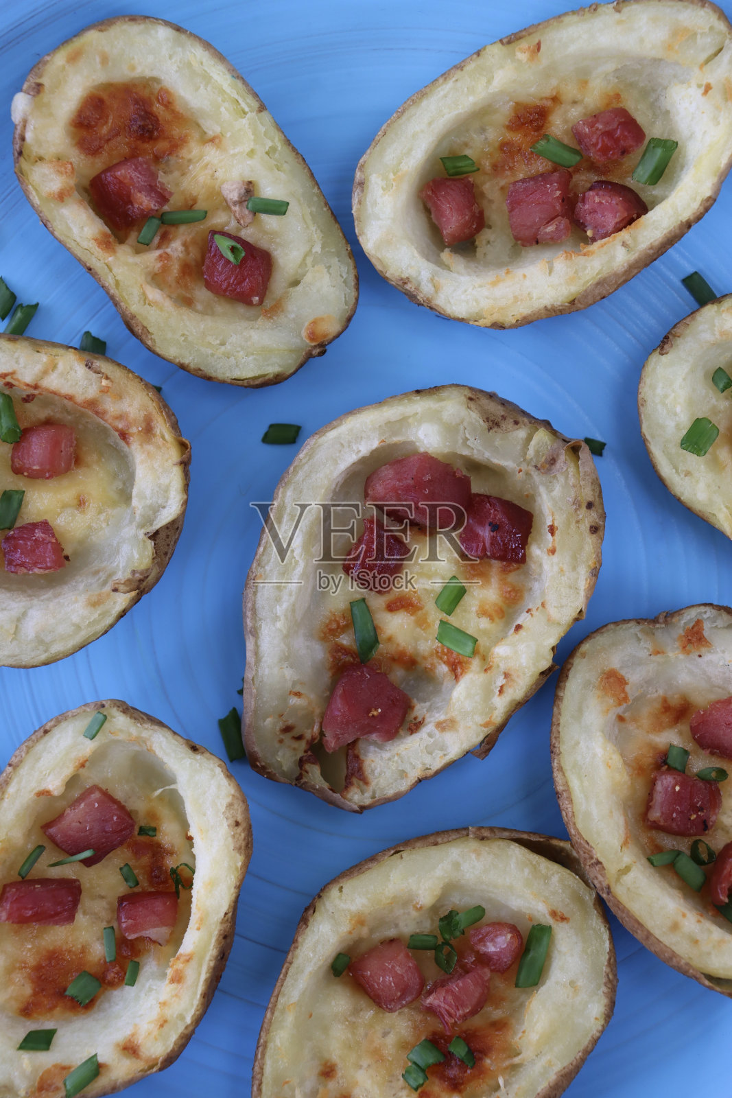 一组烤土豆皮配上融化的奶酪、熏肉块和酸奶油，点缀着切碎的韭菜，放在蓝绿色的盘子里，俯瞰美景照片摄影图片