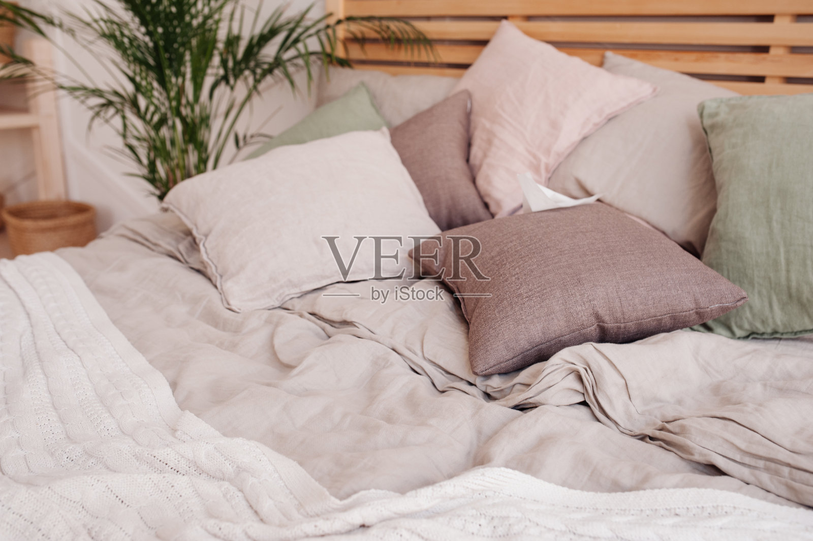 非常舒适柔和的地方放松和睡觉。柔软的栗色和绿色枕头，皱褶的米色针织毯子放在大床上。有选择性的重点照片摄影图片