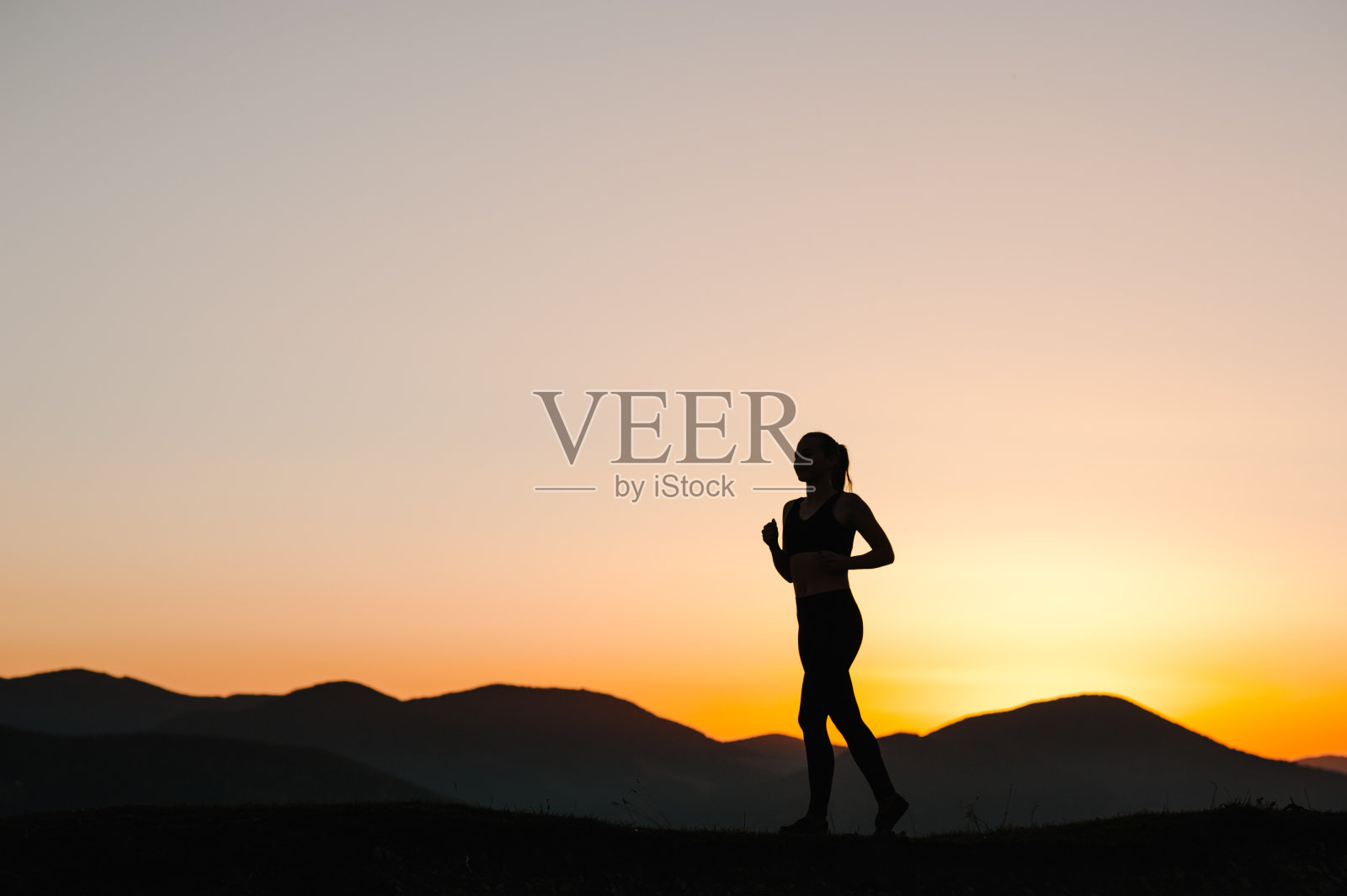 女运动员在山上的公路上跑步。日出时，奔跑时天空的剪影。跑步健身女孩在运动紧身衣。明亮的夕阳和模糊的背景。水平的。照片摄影图片