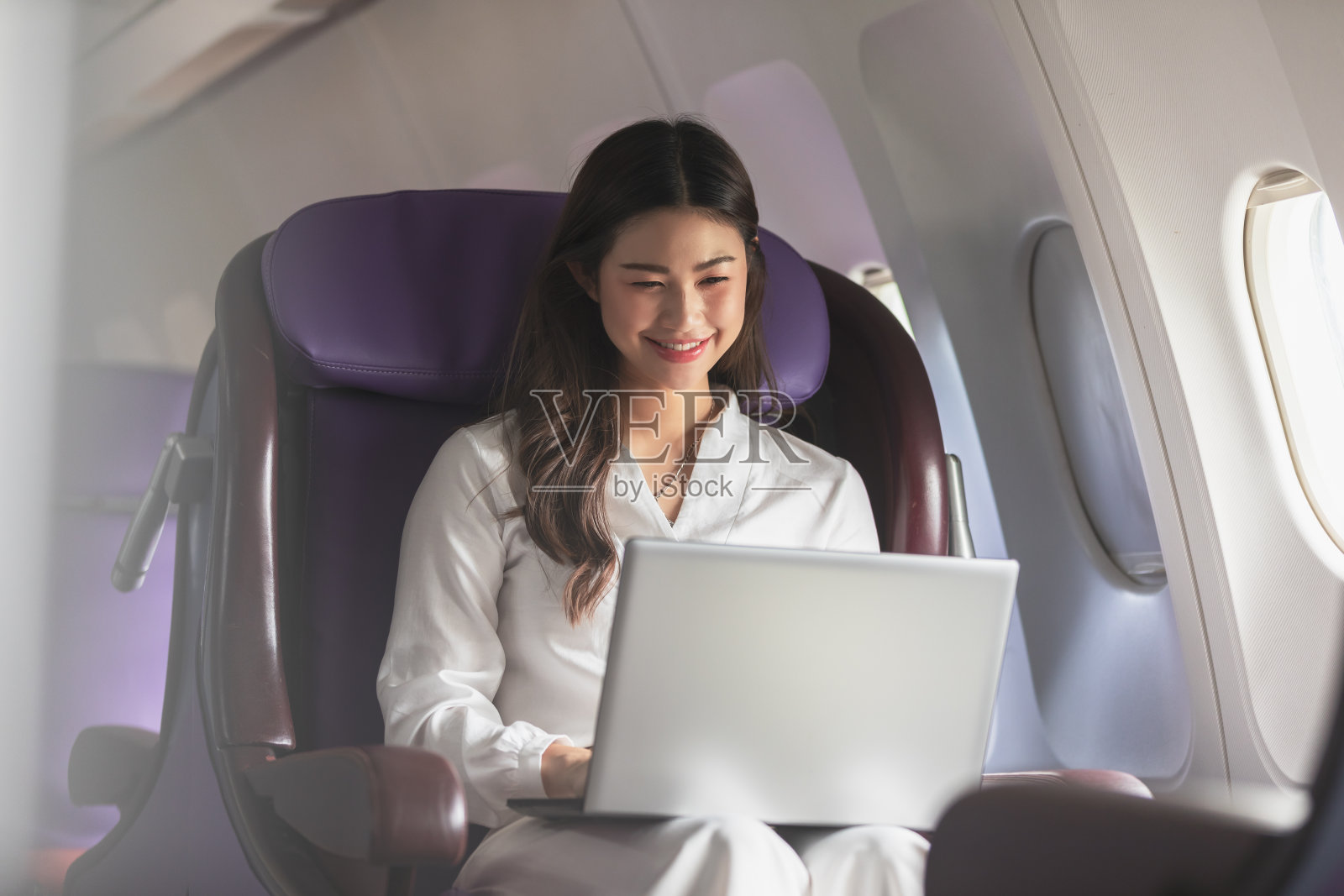 亚洲年轻女子使用笔记本电脑坐在靠近窗户的头等舱飞机在飞行，旅游和商业概念照片摄影图片