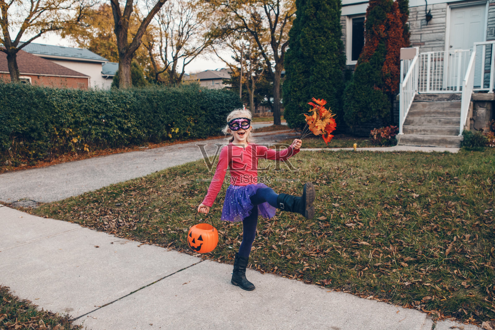 不给糖就捣蛋。快乐的女孩带着红色南瓜篮去万圣节捣蛋。可爱的孩子穿着女巫服装去邻居家要糖果和零食。照片摄影图片