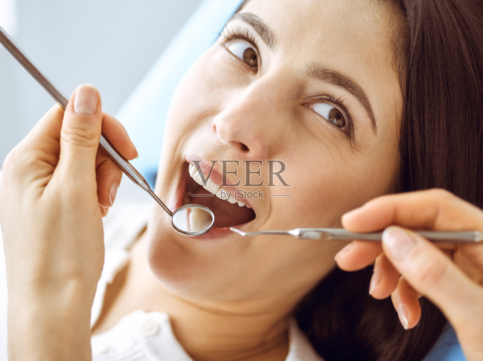 微笑的黑发女人正在检查牙医在牙科诊所。医生的手拿着牙科器械靠近病人的嘴。健康牙齿和医学理念照片摄影图片