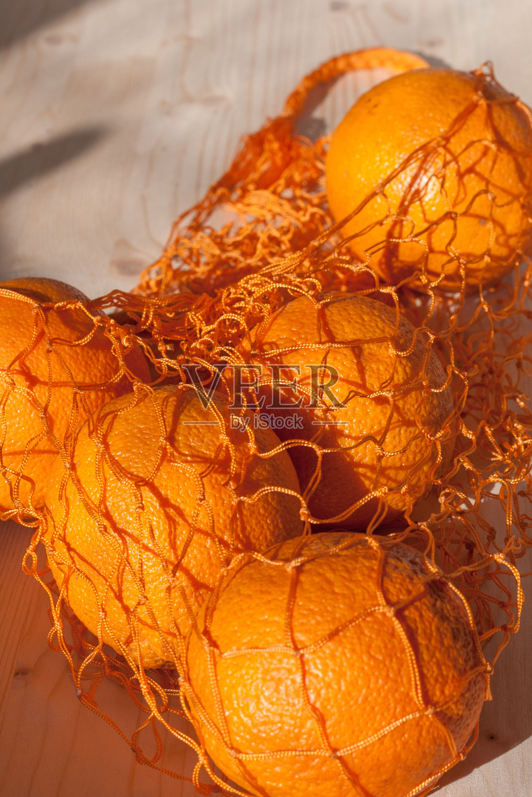 一个购物袋里的橙子放在被阳光照射的木头表面上照片摄影图片