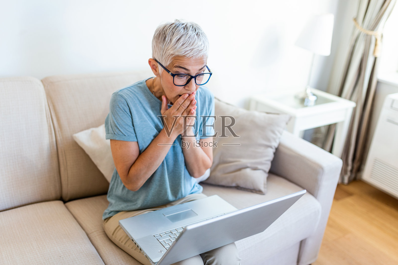 与朋友或家人视频通话时，一名高级女性看起来很惊讶。照片摄影图片